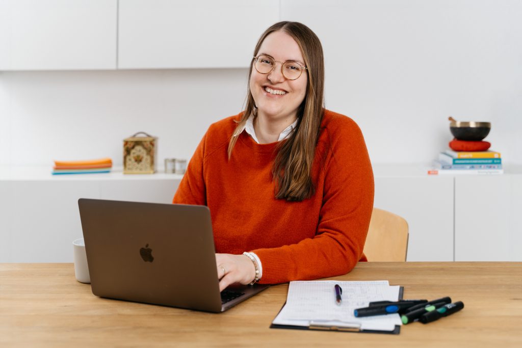 Lisa Schöffel ist Teamentwicklerin und sitzt beim Systemischen Coaching in Köln an einem Schreibtisch